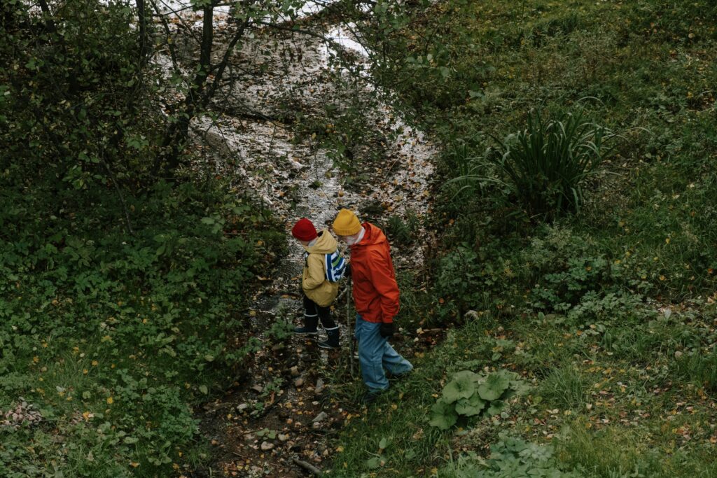 A man and a child in hats explore a forest stream, enjoying nature together.